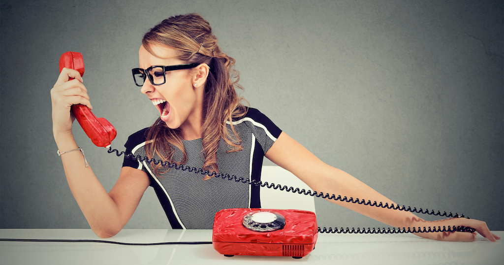 Woman looking at red telephone with an angry face.